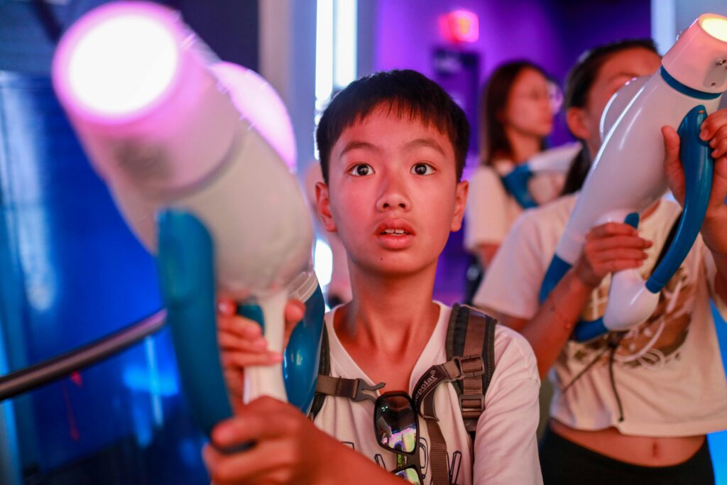 Asian boy engaged in a thrilling arcade shooting game, experiencing pure joy and focus.